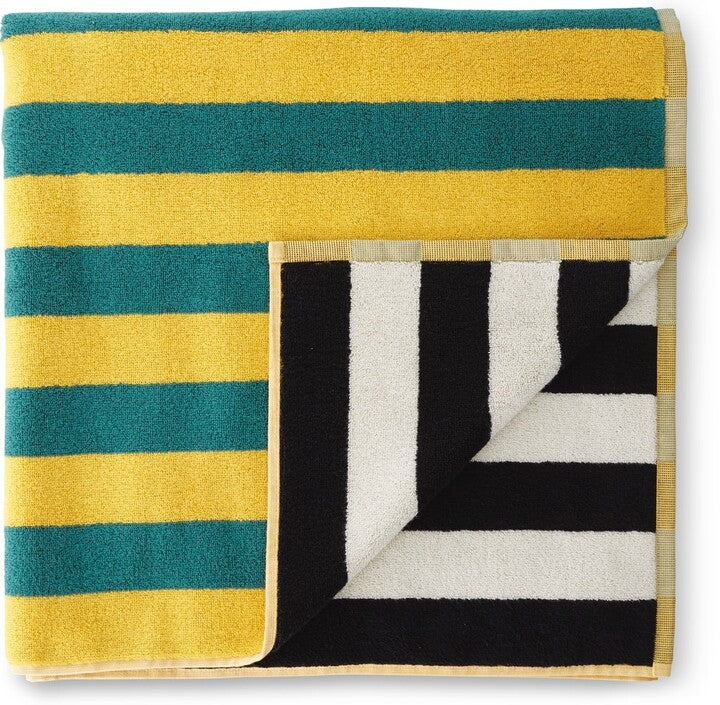 A vibrant Dusen Dusen striped beach towel in the Chincoteague pattern, spread out on sandy beach. The towel features bold, colorful stripes in various widths, creating a playful and eye-catching design. Made from soft, absorbent fabric, it’s perfect for lounging by the water or drying off after a swim, adding a stylish flair to any beach day.