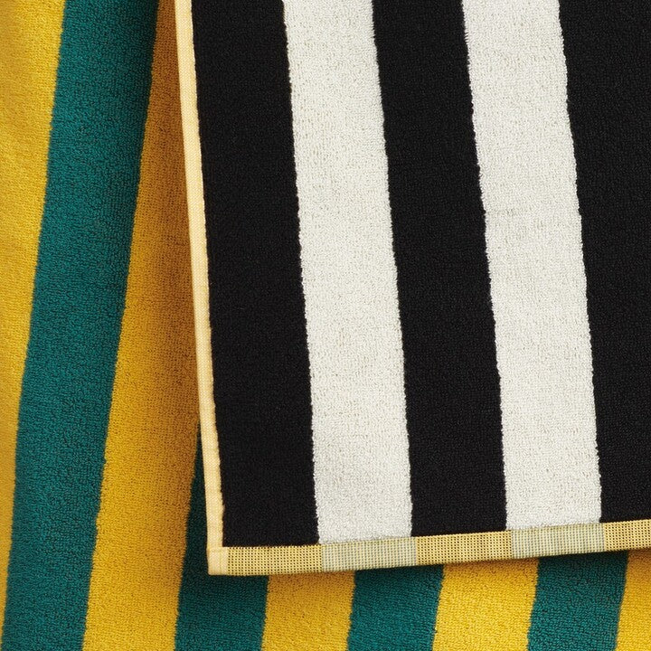 A vibrant Dusen Dusen striped beach towel in the Chincoteague pattern, spread out on sandy beach. The towel features bold, colorful stripes in various widths, creating a playful and eye-catching design. Made from soft, absorbent fabric, it’s perfect for lounging by the water or drying off after a swim, adding a stylish flair to any beach day.